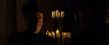 Movie still from “The Monuments Men” (2014), directed by George Clooney – A man wearing a black hat standing in front of candles in a dark room; Close Up shot, Over the shoulder angle