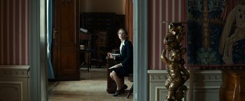 Movie still from “The Monuments Men” (2014), directed by George Clooney – A woman sitting on top of a chair in a living room; Wide shot, Low angle