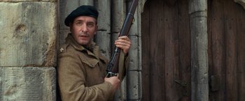 Movie still from “The Monuments Men” (2014), directed by George Clooney – A man holding a rifle while standing next to a wooden wall; Close Up shot, Low angle