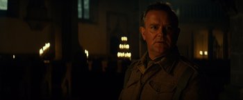 Movie still from “The Monuments Men” (2014), directed by George Clooney – A man standing in a room with a candle light in the background; Close Up shot, Over the shoulder angle