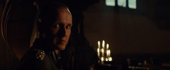 Movie still from “The Monuments Men” (2014), directed by George Clooney – A man with a bald head standing in front of candles; Close Up shot, Over the shoulder angle