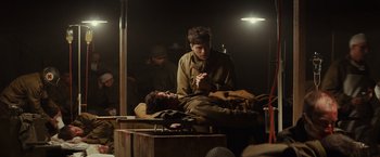 Movie still from “The Monuments Men” (2014), directed by George Clooney – A man in a military uniform is sitting on a bed while another man is standing next to him; Medium shot, Over the shoulder angle