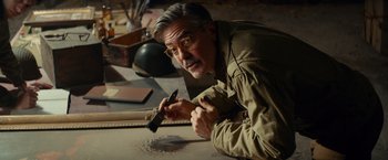 Movie still from “The Monuments Men” (2014), directed by George Clooney – A man in a tan jacket holding a pair of scissors; Medium shot, High angle