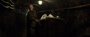 Movie still from “The Monuments Men” (2014), directed by George Clooney – A man standing next to another man in a dark room; Medium shot, Low angle