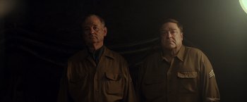 Movie still from “The Monuments Men” (2014), directed by George Clooney – A couple of men standing next to each other in a dark room; Medium shot, Low angle