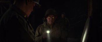 Movie still from “The Monuments Men” (2014), directed by George Clooney – An older man in a helmet and glasses holding a flashlight; Medium shot, Over the shoulder angle