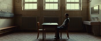Movie still from “The Monuments Men” (2014), directed by George Clooney – A man sitting at a table in front of a cell phone; Wide shot, Low angle