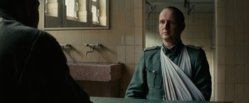 Movie still from “The Monuments Men” (2014), directed by George Clooney – A man in a uniform sitting in front of a bathroom sink; Medium shot, Over the shoulder angle