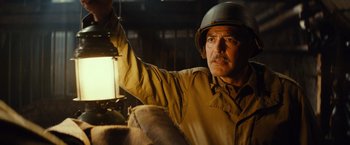 Movie still from “The Monuments Men” (2014), directed by George Clooney – An older man wearing a helmet while standing next to a lamp; Close Up shot, Low angle