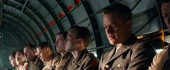 Movie still from “The Monuments Men” (2014), directed by George Clooney – A group of men in military uniforms sitting next to each other; Medium shot, Low angle