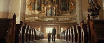 Movie still from “The Monuments Men” (2014), directed by George Clooney – A man and a child are standing in a church; Wide shot, Low angle