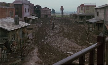 Movie still from “Django” (1966), directed by Sergio Corbucci – A dirt field with houses in the background; Extreme Wide shot, High angle