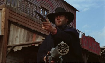 Movie still from “Django” (1966), directed by Sergio Corbucci – A man holding a gun in his hand while standing in front of a building; Medium shot, Low angle