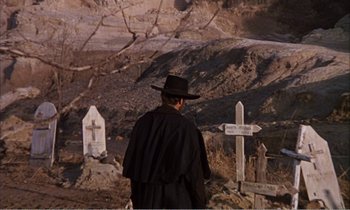 Movie still from “Django” (1966), directed by Sergio Corbucci – A man wearing a black hat standing in front of some crosses; Wide shot, Low angle