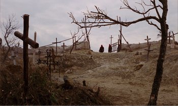 Movie still from “Django” (1966), directed by Sergio Corbucci – A person sitting on a dirt hill near a wooden fence; Extreme Wide shot, High angle