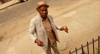 Movie still from “Do the Right Thing” (1989), directed by Spike Lee – An older man in a hat and a jacket is holding a sandwich; Medium shot, Low angle