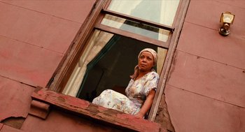 Movie still from “Do the Right Thing” (1989), directed by Spike Lee – A woman sitting on a window ledge looking out of a window; Medium shot, Low angle
