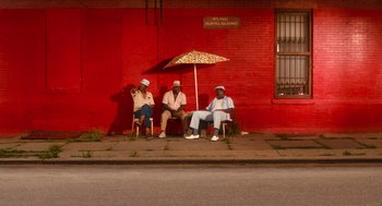 Movie still from “Do the Right Thing” (1989), directed by Spike Lee – A group of people sitting under an umbrella on the side of a building; Extreme Wide shot, Low angle