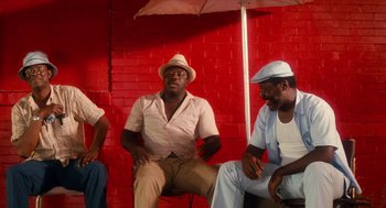 Movie still from “Do the Right Thing” (1989), directed by Spike Lee – A group of men sitting next to each other under an umbrella; Medium shot, Low angle
