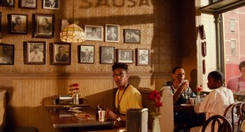 Movie still from “Do the Right Thing” (1989), directed by Spike Lee – A man sitting at a table in front of a wall of pictures; Wide shot, Low angle
