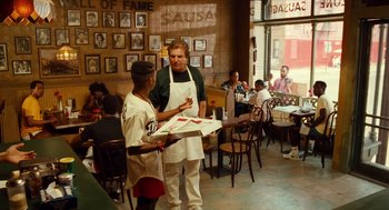 Movie still from “Do the Right Thing” (1989), directed by Spike Lee – A man standing next to another man holding a box of pizza; Wide shot, Over the shoulder angle