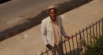 Movie still from “Do the Right Thing” (1989), directed by Spike Lee – An older man standing next to a black fence; Medium shot, Low angle