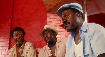 Movie still from “Do the Right Thing” (1989), directed by Spike Lee – Two men wearing hats are sitting next to each other; Close Up shot, Low angle