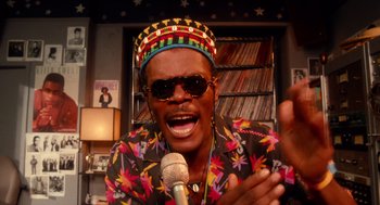 Movie still from “Do the Right Thing” (1989), directed by Spike Lee – A man wearing a hat and sunglasses is singing into a microphone; Close Up shot, Low angle