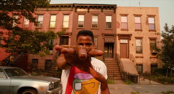 Movie still from “Do the Right Thing” (1989), directed by Spike Lee – A man holding a piece of food in front of his face; Medium shot, Low angle