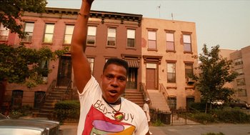 Movie still from “Do the Right Thing” (1989), directed by Spike Lee – A man in a white t - shirt raises his fist in the air; Medium shot, Low angle