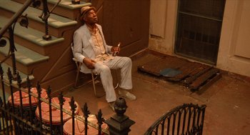 Movie still from “Do the Right Thing” (1989), directed by Spike Lee – A man sitting on a chair in front of a house; Wide shot, High angle