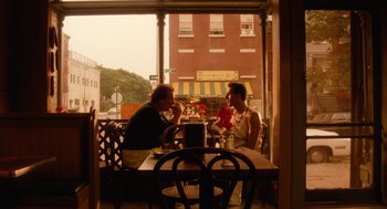Movie still from “Do the Right Thing” (1989), directed by Spike Lee – Two people sitting at a table in front of a building; Wide shot, Low angle