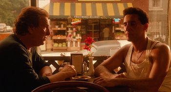 Movie still from “Do the Right Thing” (1989), directed by Spike Lee – Two men sitting at a table in front of each other at an outdoor cafe; Medium shot, Over the shoulder angle