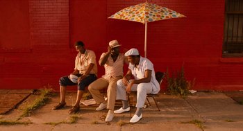 Movie still from “Do the Right Thing” (1989), directed by Spike Lee – A group of men sitting under an umbrella on a sidewalk; Wide shot, Low angle