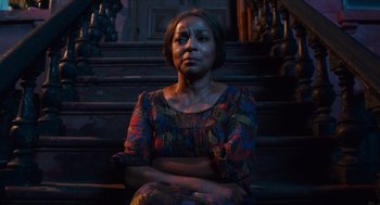 Movie still from “Do the Right Thing” (1989), directed by Spike Lee – A woman sitting on a wooden step in a dark room; Medium shot, Low angle