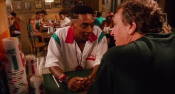 Movie still from “Do the Right Thing” (1989), directed by Spike Lee – A man sitting at a table talking to another man; Medium shot, Over the shoulder angle