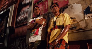 Movie still from “Do the Right Thing” (1989), directed by Spike Lee – A couple of men standing next to each other on a wall; Medium shot, Low angle