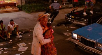 Movie still from “Do the Right Thing” (1989), directed by Spike Lee – An older man holding a little girl on the side of the road; Medium shot, High angle