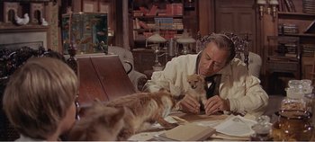 Movie still from “Doctor Dolittle” (1967), directed by Richard Fleischer – An older man sitting at a table with a dog; Medium shot, High angle