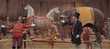 Movie still from “Doctor Dolittle” (1967), directed by Richard Fleischer – A man in a suit and top hat standing in front of an elephant and a horse; Wide shot, Low angle