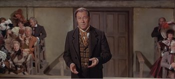 Movie still from “Doctor Dolittle” (1967), directed by Richard Fleischer – A man in a suit and tie standing in front of a wall; Medium shot, Low angle