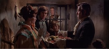 Movie still from “Doctor Dolittle” (1967), directed by Richard Fleischer – A group of people sitting around a table with food; Medium shot, Over the shoulder angle