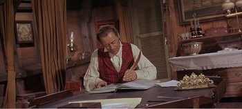 Movie still from “Doctor Dolittle” (1967), directed by Richard Fleischer – A man in a red vest is writing on an open book; Medium shot, High angle