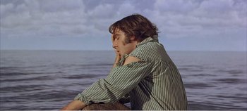 Movie still from “Doctor Dolittle” (1967), directed by Richard Fleischer – A man sitting on the ground near a body of water; Medium shot, High angle