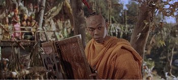 Movie still from “Doctor Dolittle” (1967), directed by Richard Fleischer – A man in a yellow robe with an elaborate hairdo; Medium shot, High angle