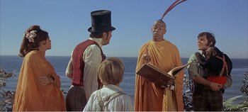 Movie still from “Doctor Dolittle” (1967), directed by Richard Fleischer – A man in an orange robe talking to two men in a top hat; Medium shot, Over the shoulder angle