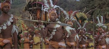 Movie still from “Doctor Dolittle” (1967), directed by Richard Fleischer – A group of men in costumes holding a bamboo stick; Medium shot, High angle
