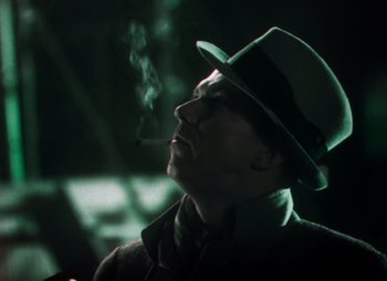 Movie still from “Doctor X” (1932), directed by Michael Curtiz – A man in a hat and a tie smoking a cigarette; Close Up shot, Low angle