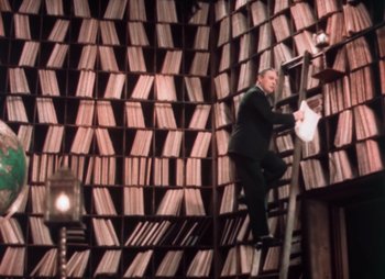 Movie still from “Doctor X” (1932), directed by Michael Curtiz – A man in a suit climbing up a ladder to a book shelf; Wide shot, Low angle