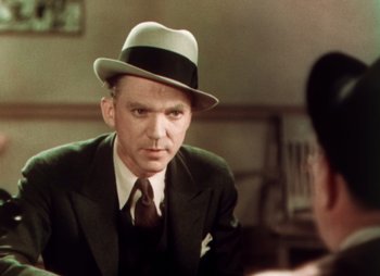 Movie still from “Doctor X” (1932), directed by Michael Curtiz – A man wearing a suit and a hat in front of a mirror; Close Up shot, Over the shoulder angle